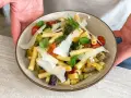Un piatto di pasta fredda gourmet con verdure miste, pomodorini, basilico e scaglie di parmigiano.