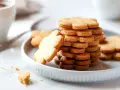 Una pila di biscotti pasta frolla a forma di fiore su un piatto bianco, con una tazza di caffè sullo sfondo.