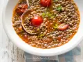 Una ciotola di zuppa di lenticchie veloce con pomodorini e prezzemolo fresco. Un cucchiaio serve la gustosa zuppa.