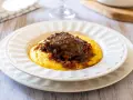 Guancette di maiale brasate su un letto di polenta cremosa, un piatto ricco e saporito.