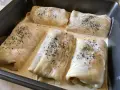 Crespelle farina di ceci ripiene, pronte per essere infornate, immerse in una cremosa besciamella e cosparse di pepe nero.