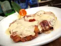 Cotoletta alla bolognese dorata e filante, con prosciutto e formaggio fuso, servita su un piatto bianco con contorno di purè e carota.