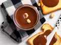 Crema di nocciole fatta in casa in un barattolo, con fette biscottate e nocciole sparse.