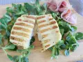 Toast di patate grigliato, ripieno di prosciutto e formaggio filante, servito su un letto di insalata fresca.