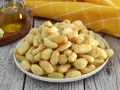 Gnocchi dorati e croccanti, cotti nella friggitrice ad aria, conditi con erbe aromatiche. Accanto, olio d'oliva e gnocchi crudi.