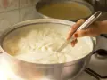 Una mano mescola un cremoso yogurt fatto in casa con fermenti in una ciotola d'acciaio su un fornello.