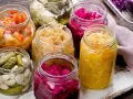 Vasi di vetro pieni di cibi fermentati fatti in casa: crauti, cavolo rosso, cetriolini e verdure miste.