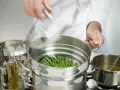 Asparagi freschi pronti per la cottura al vapore in una vaporiera. Un cuoco sta per coprire il cestello.