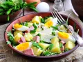 Deliziosa insalata di patate estiva con uova sode, salumi, formaggio e erbe fresche, servita in una ciotola di terracotta.