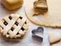 Preparazione di crostatine con pasta frolla classica. Stesa di impasto, formine a cuore e una crostatina già pronta.