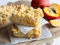 Sbriciolata pesche e amaretti: due fette impilate su carta forno, con pesche fresche sullo sfondo.