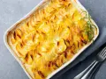 Delizioso millefoglie di patate dorate e croccanti, cotto in una teglia bianca, guarnito con rosmarino fresco e pepe nero.