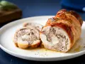 Coniglio in porchetta, un rotolo di carne succulento e profumato, tagliato a fette su un piatto bianco.