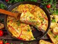 Frittata di peperoni dorata in padella, con fette di pane tostato e pomodorini freschi.