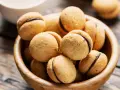 Baci di dama ricetta: deliziosi biscotti alle nocciole con ripieno di cioccolato, serviti in una ciotola di legno.