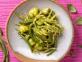 Un piatto invitante di trofie al pesto, con fagiolini e patate, su uno sfondo rosa vibrante.