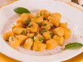 Gnocchi di zucca dorati e soffici, guarniti con basilico fresco e una spolverata di pangrattato croccante, serviti su un piatto bianco.