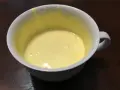 Una tazza bianca contiene un composto giallo pallido, un uovo sbattuto con zucchero, pronto per essere cucinato.
