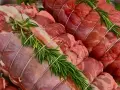 Due **tagli di carne per arrosto** pronti per essere cucinati, legati con spago e guarniti con rametti di rosmarino fresco.