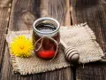 Un vasetto di miele ambrato, un fiore giallo e un cucchiaio di legno su tela grezza. La differenza tra miele e melata è un mistero da svelare.