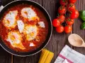 Uova al pomodoro in padella, con pomodorini freschi, basilico e un cucchiaio di legno.