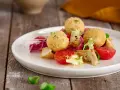 Sfere dorate di miglio fritte, servite con un'insalata fresca di pomodorini, radicchio e pollo. Un'idea gustosa per le tue ricette con miglio.