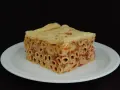 Un pezzo di timballo di pasta con ragù e pasta cotta al forno, servito su un piatto bianco.