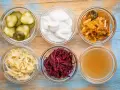 Sei ciotole di vetro con cetrioli, yogurt, kimchi, crauti, barbabietole e brodo, ingredienti per probiotici naturali fatti in casa.