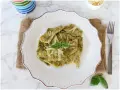 Testaroli al pesto, un piatto tradizionale ligure, servito su un piatto bianco con formaggio grattugiato e basilico fresco.