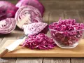 Cavolo cappuccio rosso affettato in una ciotola di vetro e su un tagliere, con cavoli interi e tagliati a spicchi sullo sfondo.