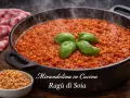 A cast iron pan filled with steaming soy ragu, garnished with basil leaves. A small bowl of dry soy granules is in the foreground.