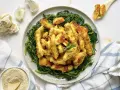 Luganega al forno croccante su letto di verdure verdi. Accanto, aglio e pangrattato.