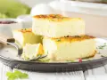 Fetta di frittata al forno soffice e alta, guarnita con erbe aromatiche, su un piatto scuro.