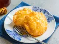 Due dolci sardi fritti, dorati e lucidi di miele, su un piatto blu e bianco con una forchetta.
