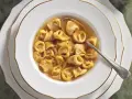 Un primo piatto fumante: tortellini in brodo, un classico della tradizione culinaria italiana, serviti in una ciotola bianca con bordo dorato.