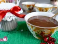 Un vasetto decorato con un fiocco rosso e una tazza piena di cioccolata fatta in casa, pronta per essere gustata.
