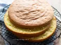 Due dischi di pan di spagna torta, uno sopra l'altro, su una griglia. La superficie è dorata e soffice, pronta per essere farcita.