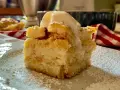 Una fetta di torta di pane raffermo mele e uvetta, cosparsa di zucchero a velo e sormontata da una pallina di gelato.
