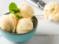Coppa di cremoso gelato alla vaniglia, guarnita con foglioline di menta fresca. Sullo sfondo, un cucchiaio da gelato pieno.