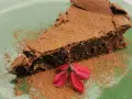 Una fetta di torta tenerina vegana, cosparsa di cacao, con un fiore rosso su un piatto verde.