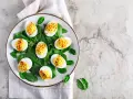 Uova sode ricette sfiziose: uova ripiene su letto di spinaci, guarnite con paprika.