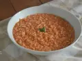 Un cremoso riso al pomodoro veloce, guarnito con una fogliolina verde, servito in una ciotola bianca su una tovaglia a quadri.