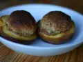 Due pesche ripiene senza amaretti, cotte al forno, servite in una ciotola bianca su un tavolo di legno.