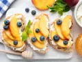 Bruschette con pesche mature, ricotta e mirtilli. Un'idea fresca per ricette con pesche mature, perfetta per la colazione o uno spuntino leggero.