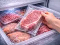 Mano che prende una bistecca sottovuoto dal freezer. Varie confezioni di carne congelata, tra cui macinato e pezzi interi, pronte per essere scongelate.