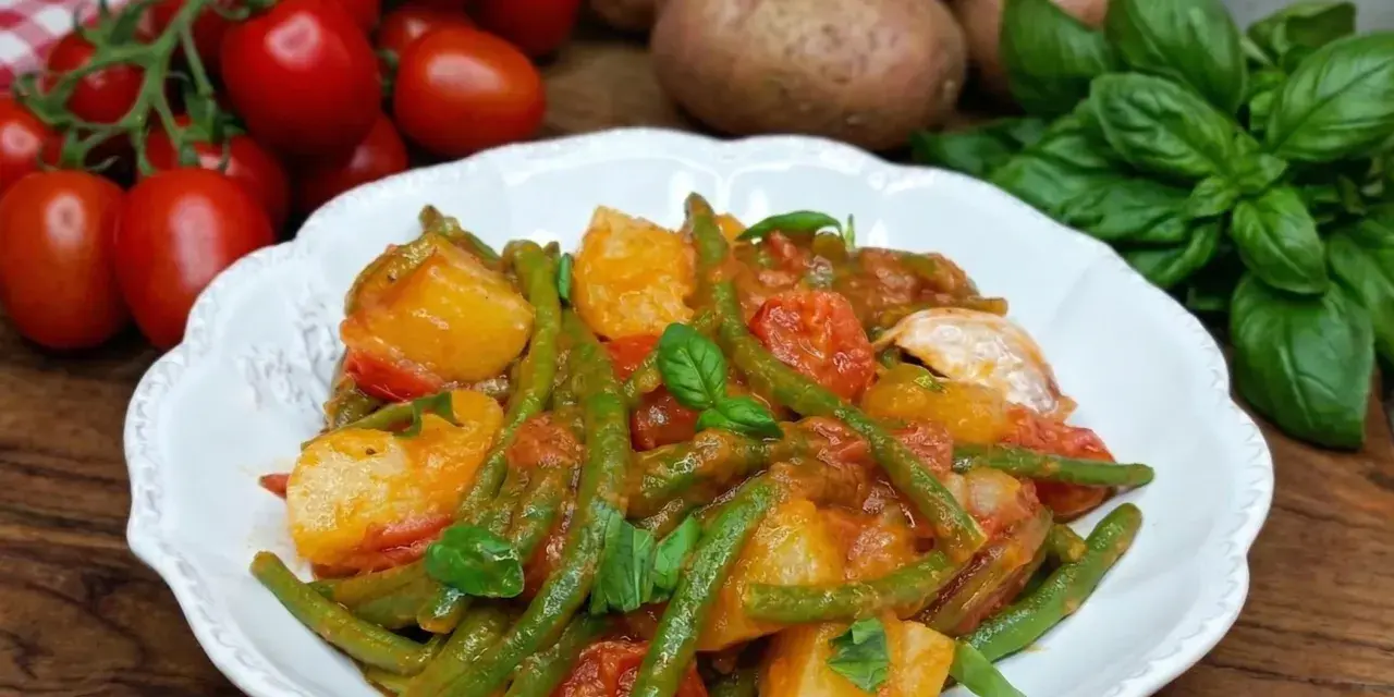 Un piatto di fagiolini e patate alla pugliese, con pomodorini freschi e basilico, pronto per essere gustato.