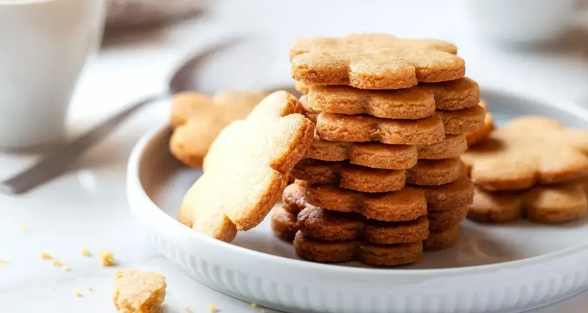 Una pila di biscotti pasta frolla a forma di fiore su un piatto bianco, con una tazza di caffè sullo sfondo.