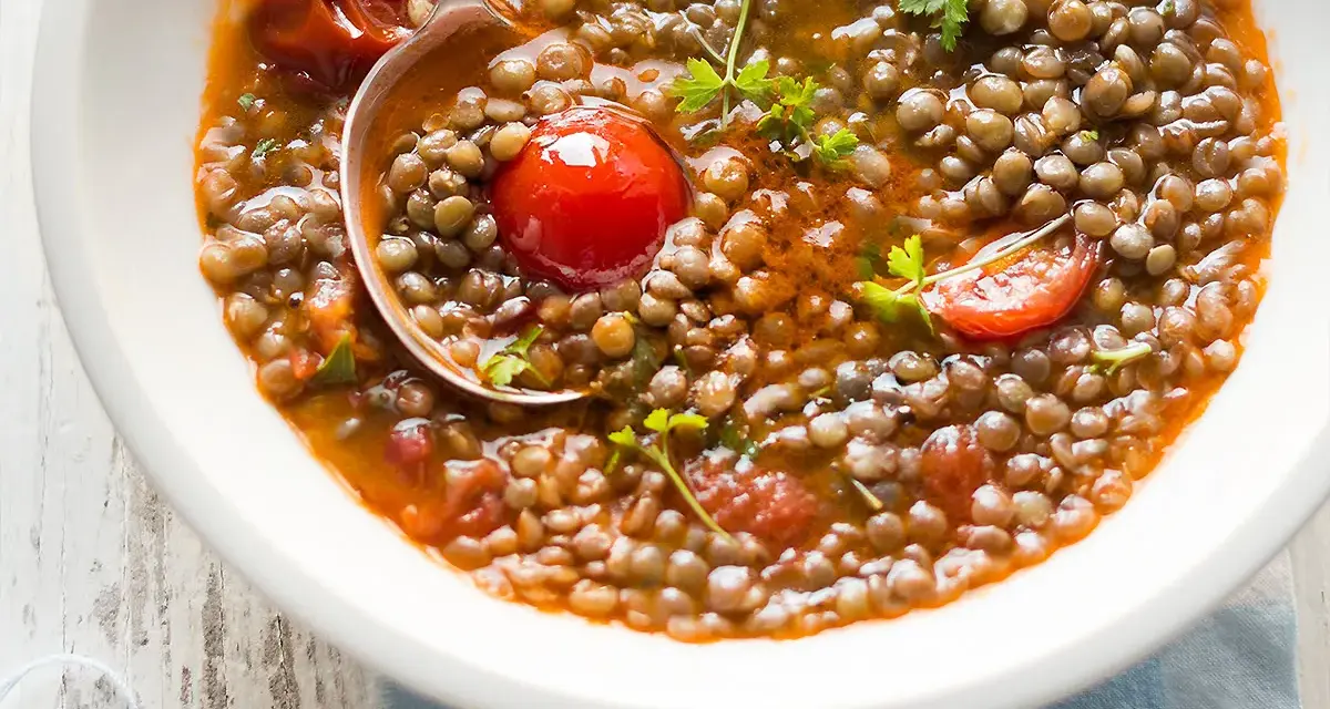 Una ciotola di zuppa di lenticchie veloce con pomodorini e prezzemolo fresco. Un cucchiaio serve la gustosa zuppa.