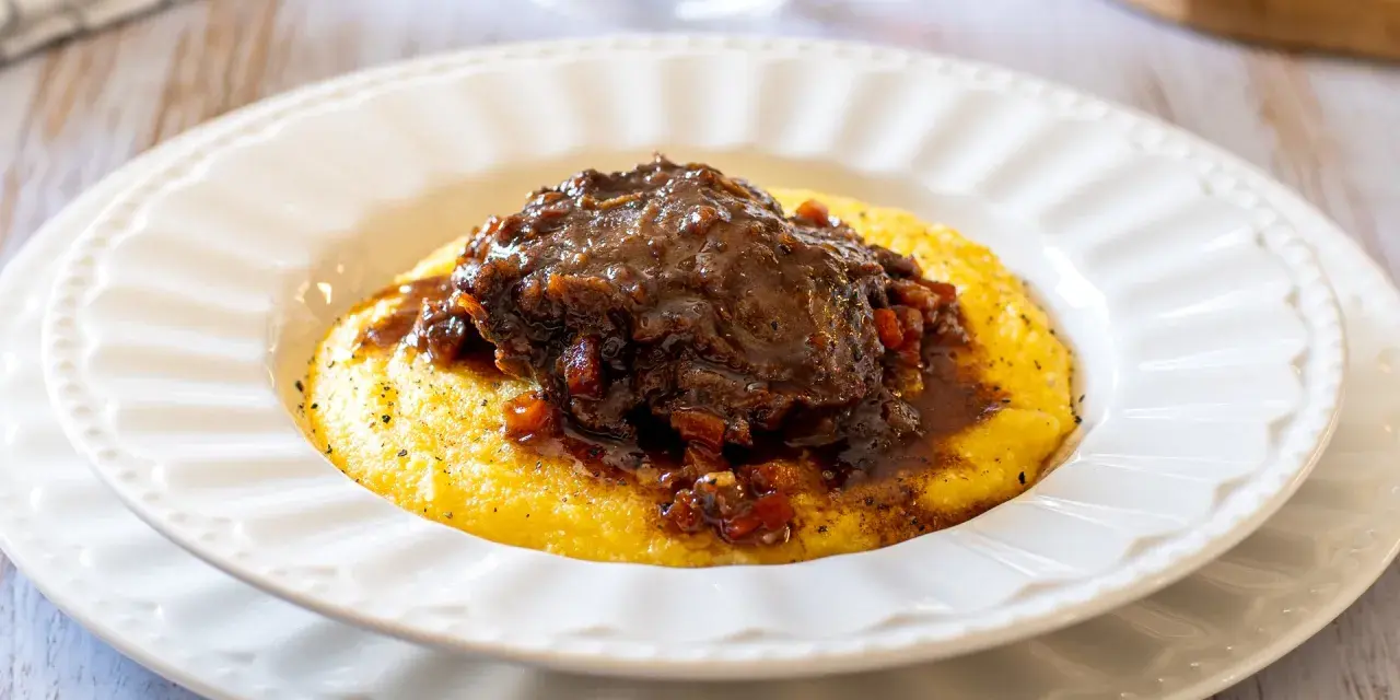 Guancette di maiale brasate su un letto di polenta cremosa, un piatto ricco e saporito.
