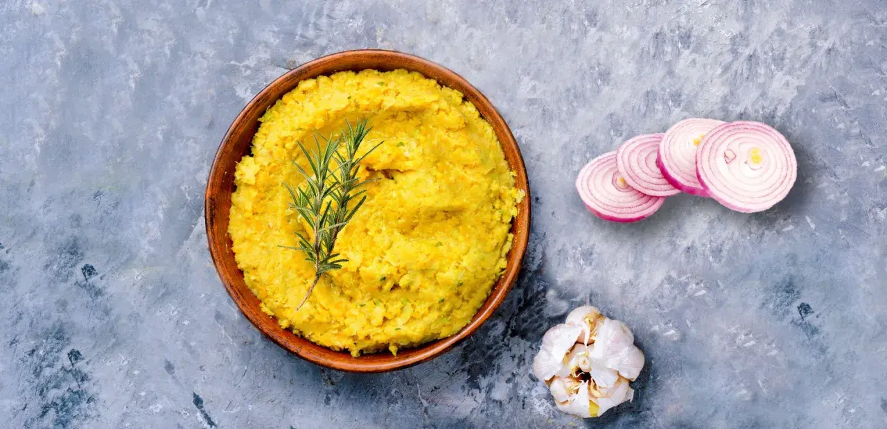 Piatto di lenticchie decorticate cremose, guarnito con rosmarino, cipolla rossa affettata e aglio.